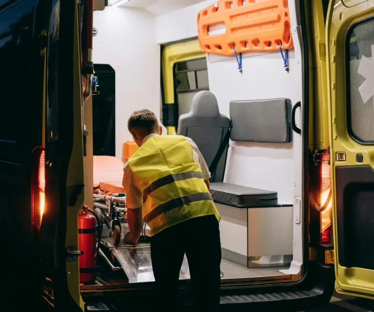 A paramedic wearing a reflective vest loads a gurney into an ambulance at night, highlighting emergency response.