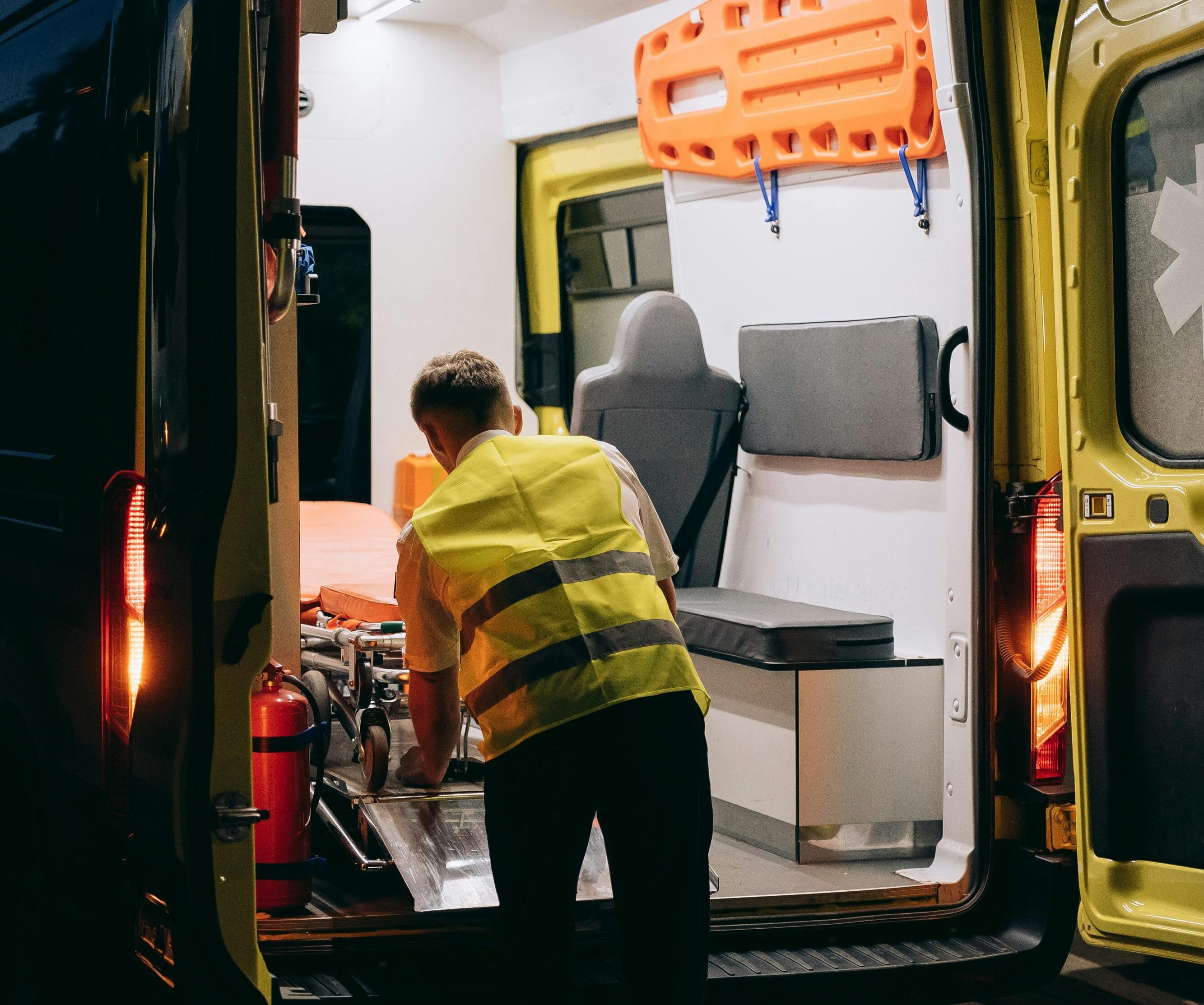 A paramedic wearing a reflective vest loads a gurney into an ambulance at night, highlighting emergency response.